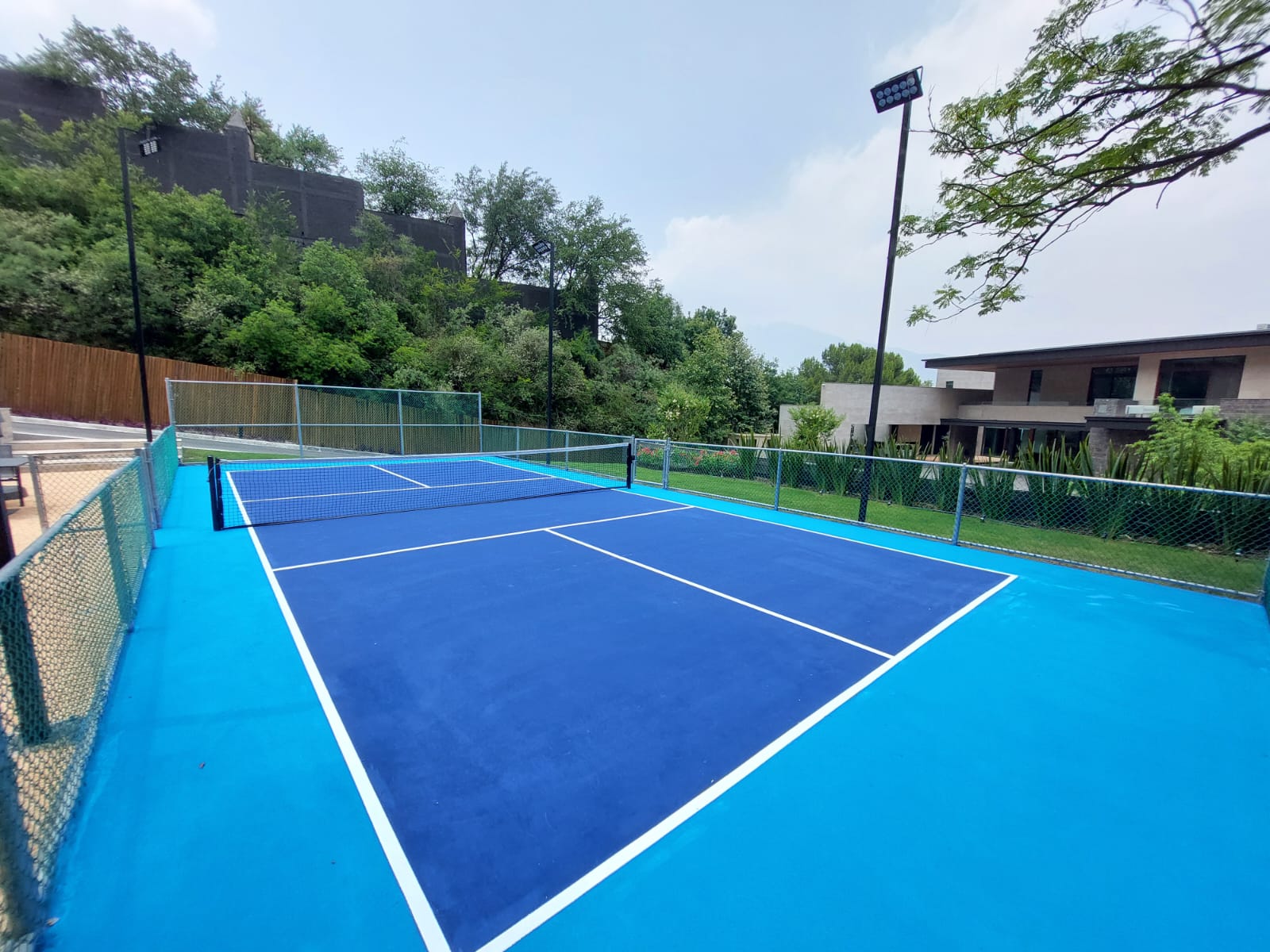 Cancha de pickleball residencial premium construida por CanchasdePickleball.mx en Nuevo León con pintura azul Laykold e iluminación LED